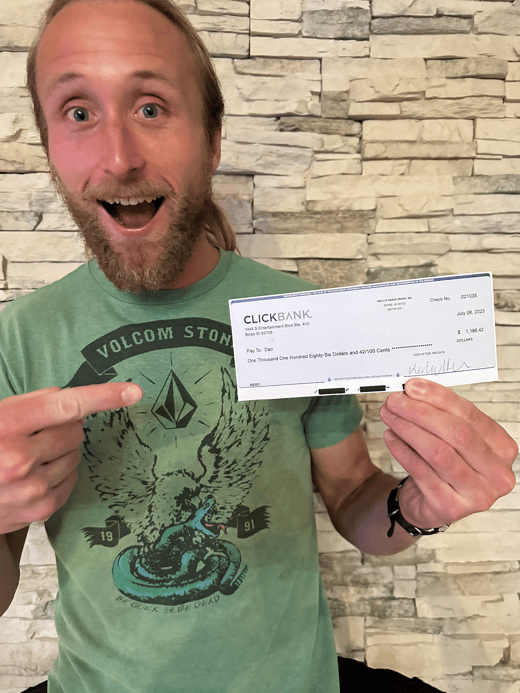 A man in a green shirt pointing to a ClickBank paycheck excitedly