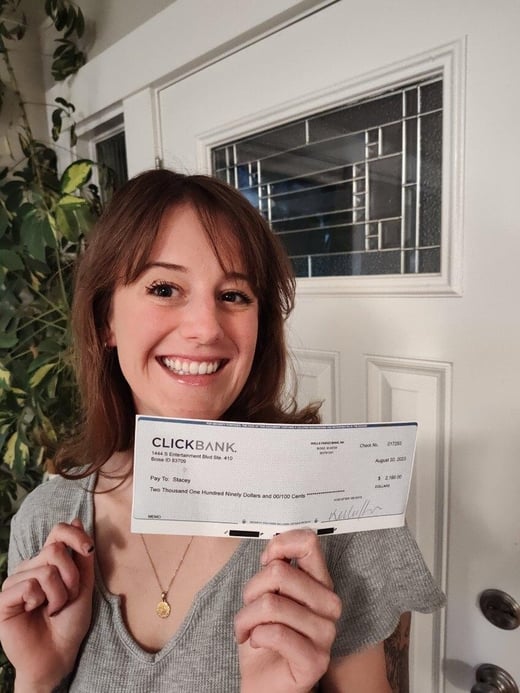 A woman in a grey shirt holding a ClickBank paycheck 